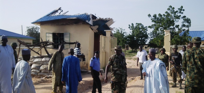 Nigerian government officials stand next to a house damaged by a Boko Haram attack Nigerian government officials stand next to a house damaged by a Boko Haram attack