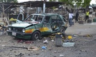 People walk past a damaged car at the site of a bomb explosion in Maiduguri, Nigeria, Friday, July 31, 2015.
