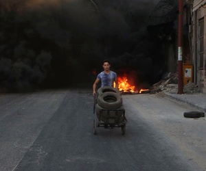 This July. 31, 2016 photo, provided by the Syrian anti-government activist group Aleppo Media Center (AMC), shows a Syrian young man burns tyres in an attempt to prevent airstrikes above Aleppo, Syria. 