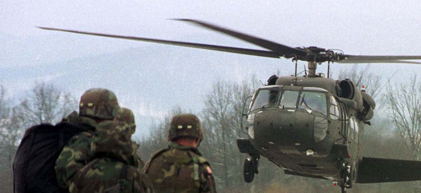 Two U.S. soldiers, members of the NATO mission to Bosnia, wait to board a helicopter, on February 14, 1999. 