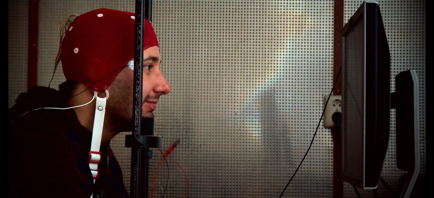 A man wears an EEG cap and stares into a computer screen as part of an experiment with brain-computer interfacing. 
