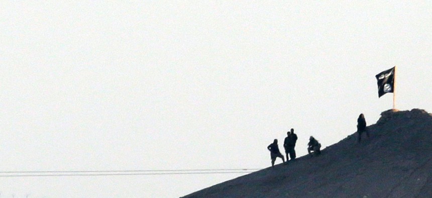 In this telephoto image shot through haze from the outskirts of Suruc at the Turkey-Syria border, ISIL militants are seen after placing their group's flag on a hilltop at the eastern side of the town of Kobani, Syria, Oct. 6, 2014. 