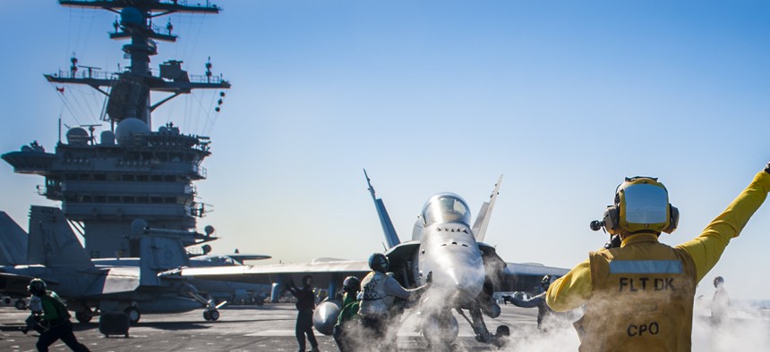 A Royal Navy Chief directs an F/A 18 Hornet onto a catapult on the flight deck of the USS Carl Vinson, on January 1, 2015.