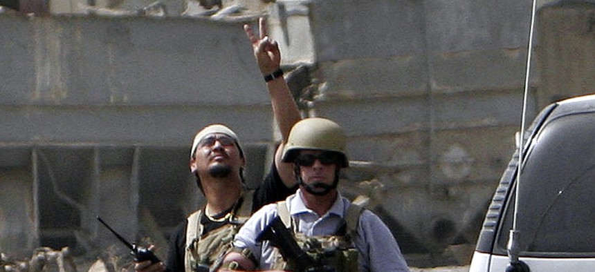 A private contractor gestures to his colleagues flying over in a helicopter as they secure the scene of a roadside bomb attack in Baghdad, Iraq, on July 5, 2005.