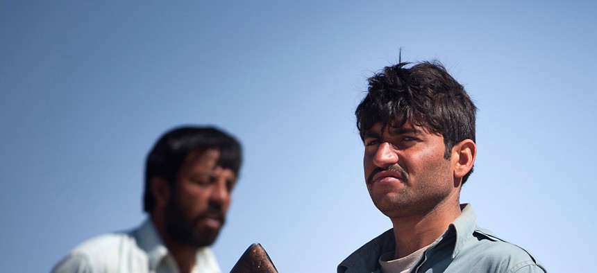An Afghan National Policeman waits for vehicles while U.S. Marines discuss a local man stopped during an operation in Garmsir District, Afghanistan, March 21, 2012.