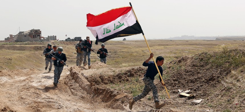 A member of the Iraqi security forces runs to plant the national flag as they surround Tikrit during clashes to regain the city from Islamic State militants.