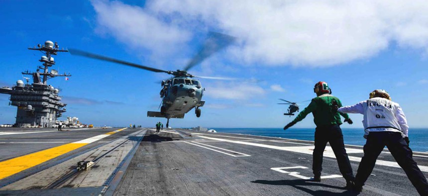 A couple of Navy enlisted personnel direct an MH-60S Knight Hawk helicopter as it prepares to land aboard the USS John C. Stennis. 