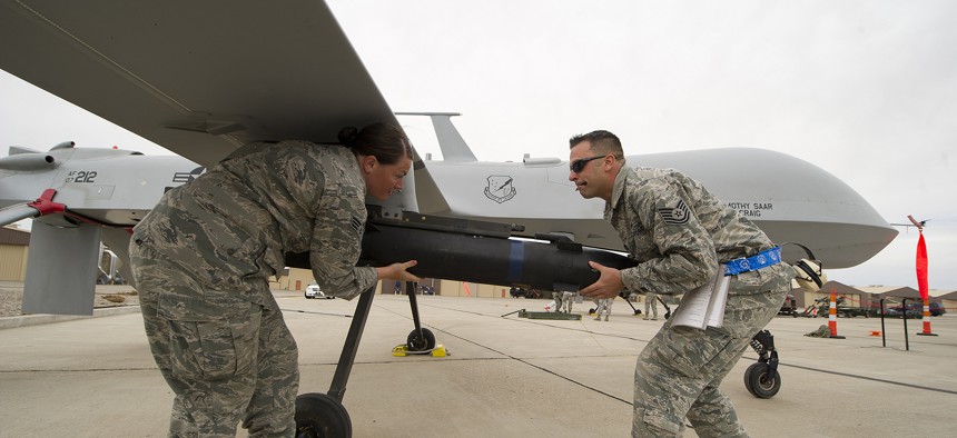 Two Air Force NCOs load munitions on an MQ-9 Predator. 