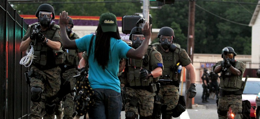 In this Aug. 11, 2014 photo, police wearing riot gear point their weapons before arresting a man in Ferguson, Mo.