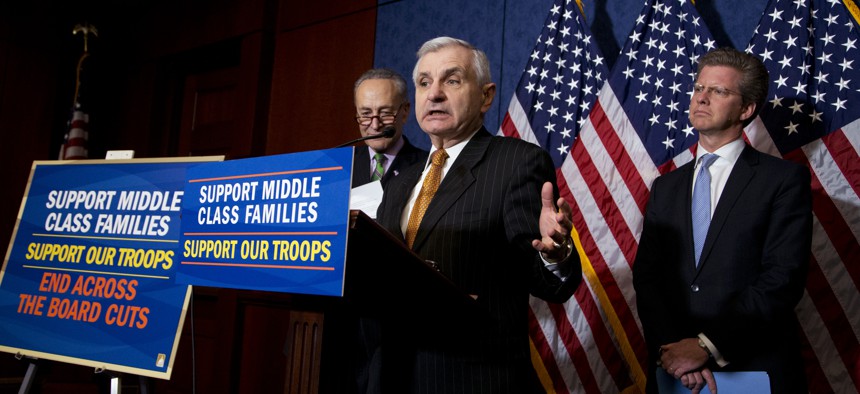 Sen. Jack Reed, D-R.I., center, with Sen. Chuck Schumer, D-N.Y., back left, and Office of Management and Budget Director Shaun Donovan, right, speaks to reporters during a news conference on Capitol Hill, on March 12, 2015.