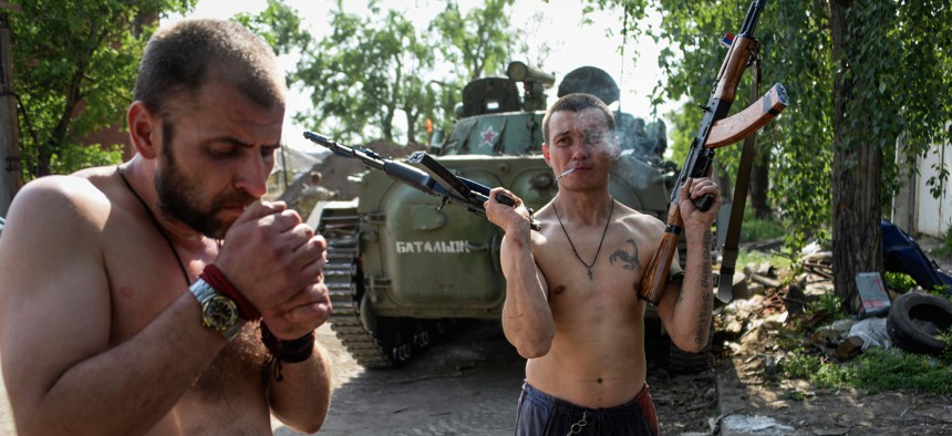 A Russia-backed rebel smokes, holding rifles in his both hands, on the outskirts of Donetsk, eastern Ukraine, Tuesday, May 26, 2015. 