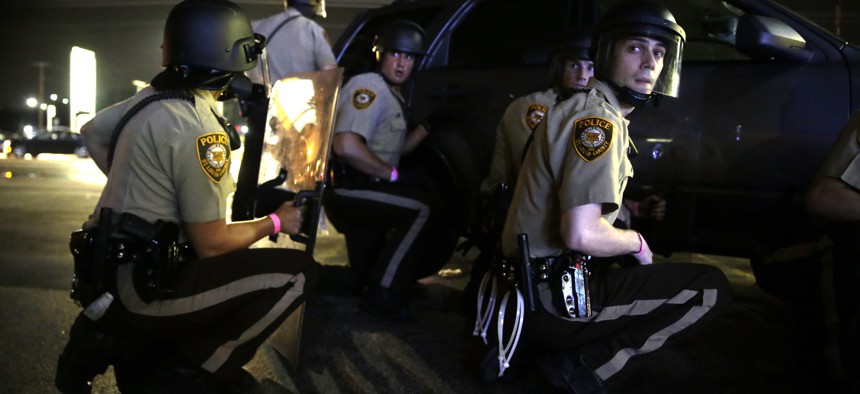 Police take cover behind a vehicle during a protest in Ferguson, Mo., Sunday, Aug. 9, 2015.