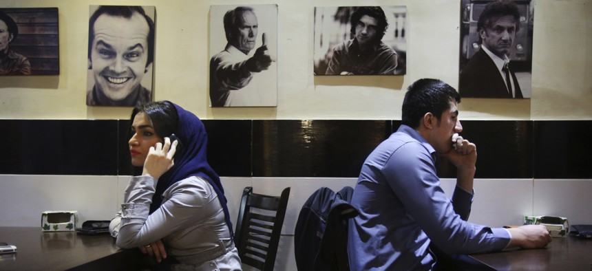 Young Iranian adults sit at a cafe, backdropped, with pictures of Western celebrities in Tehran, Iran.