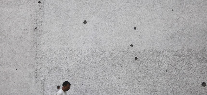 An Indian border villager walks past a house wall with mortar shell damage in Ranbir Singh Pura, 23 miles from Jammu, India.