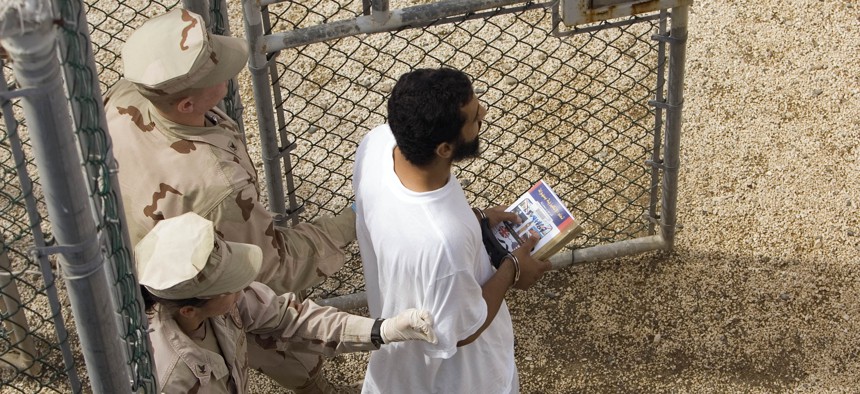 In this file photo, reviewed by the U.S. Military, guards escort a detainee carrying a book from the library trailer to the detention facility in an open air common area at Camp Delta 4 in Guantanamo Bay.