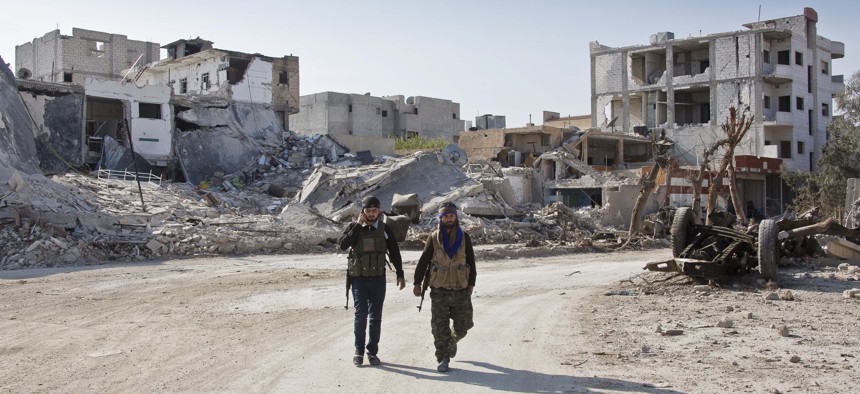 In this Wednesday, Nov. 19, 2014 photo, Kurdish People's Protection Units (YPG) soldiers walk near the town entrance circle heading to their strongholds in Kobani, Syria.