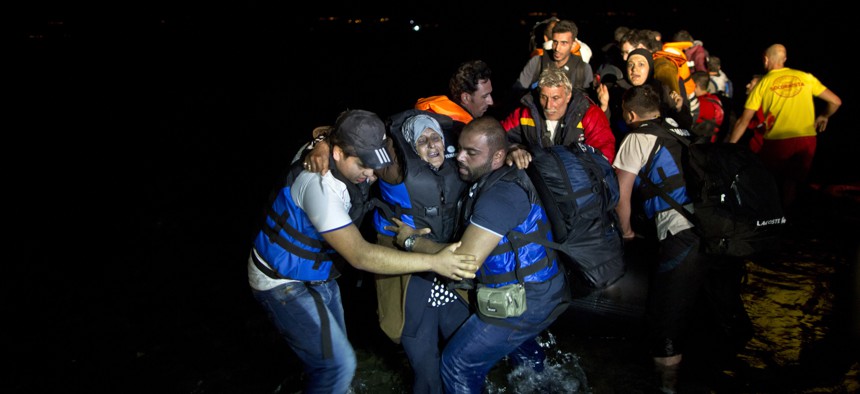Two Syrian refugees try to carry an elderly woman off a dinghy as it arrives from the Turkish coast to the northeastern Greek island of Lesbos, Tuesday, Oct. 6 , 2015.