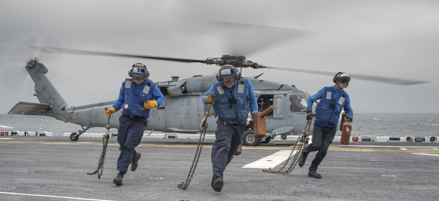 Three aviation boatswain's mates (handling) from the amphibious assault ship USS Wasp (LHD 1) and USS Bataan (LHD 5) conduct a chock and chain evolution with an SH-60 Sea Hawk aboard Wasp.