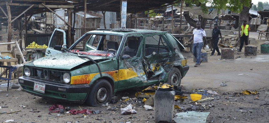People walk past a damaged car at the site of a bomb explosion in Maiduguri, Nigeria, Friday, July 31, 2015.