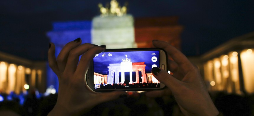 A woman takes a picture of the Brandenburg Gate, illuminated in the French national colors for the victims killed in the Friday's attacks in Paris, France in Berlin, Saturday, Nov. 14, 2015. 