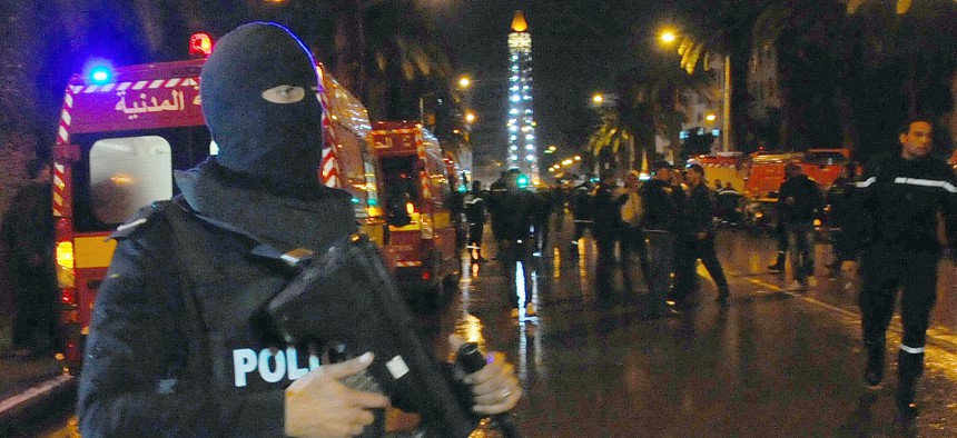 A hooded police officer prevents media from aproaching the scene of a bus explosion in the center of the capital, Tunis, Tunisia, Tuesday, Nov. 24, 2015.