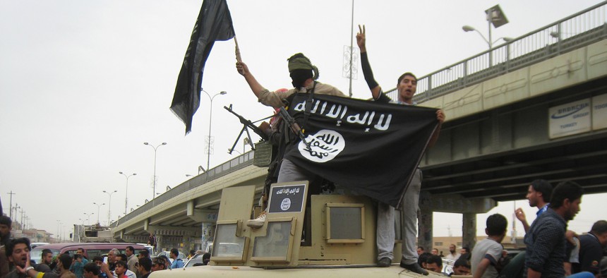 In this Sunday, March 30, 2014, file photo, Islamic State group militants hold up their flag as they patrol in a commandeered Iraqi military vehicle in Fallujah.