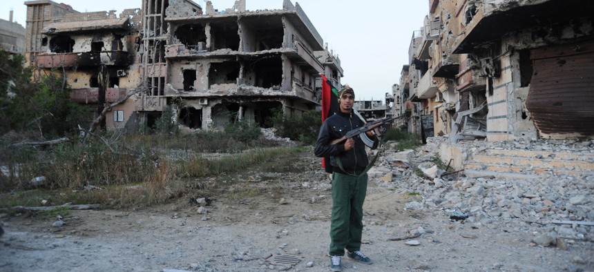 n this Feb. 23, 2016 file photo, a civilian fighter holding the Libyan flag stands in front of damaged buildings in Benghazi, Libya. The U.S., Europe and U.N. have all pinned their hopes for resolving Libya’s chaos and blocking the Islamic State group’s g