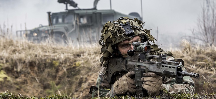 Latvian soldier looks down the barrel of his weapon with a Humvee for protection in the background, April 15, 2015.
