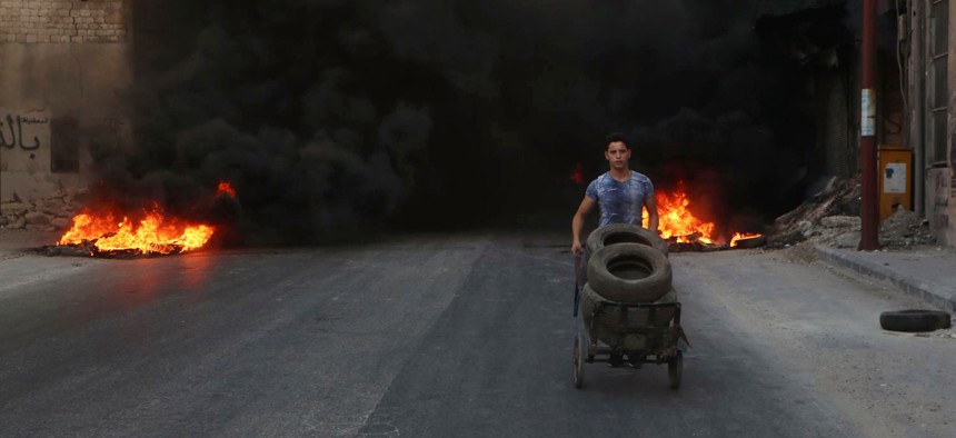 This July. 31, 2016 photo, provided by the Syrian anti-government activist group Aleppo Media Center (AMC), shows a Syrian young man burns tyres in an attempt to prevent airstrikes above Aleppo, Syria. 