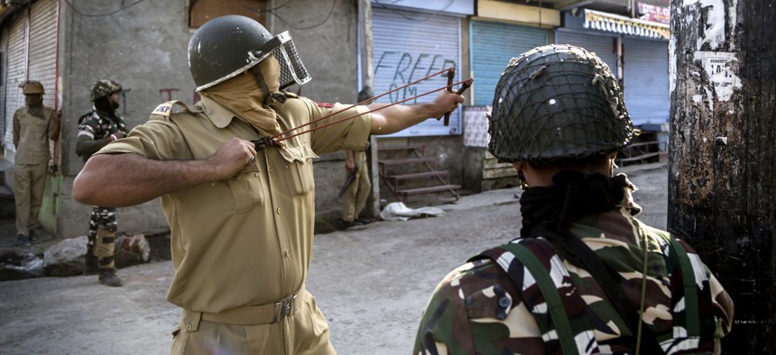 An Indian policeman uses a sling to shoot glass marbles at Kashmiri protesters during a protest in Srinagar, Indian controlled Kashmir, Friday, Oct. 7, 2016.
