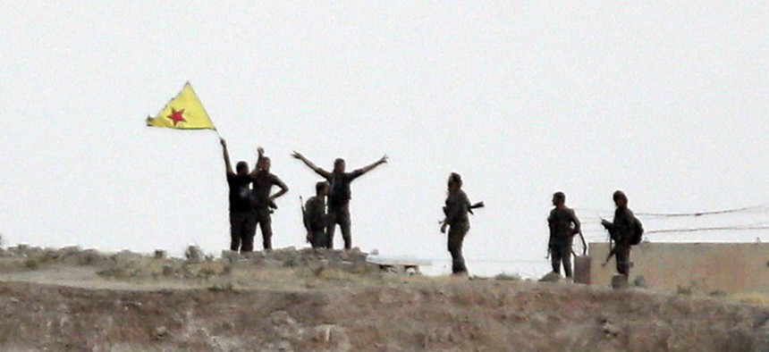 Kurdish fighters with the Kurdish People's Protection Units, or YPG, wave their yellow triangular flag in the outskirts of Tal Abyad, Syria, June 15, 2015.