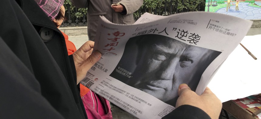In this Nov. 10, 2016 file photo, a Chinese man holds up a Chinese newspaper with the front page photo of U.S. President-elect Donald Trump and the headline "Outsider counter attack" at a newsstand in Beijing, China. 