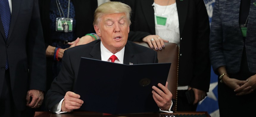 United States President Donald Trump (C) reads from one of the four executive orders he signed during a visit to the Department of Homeland Security January 25, 2017 in Washington, DC. 
