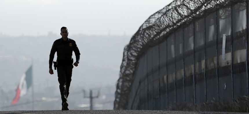 Border Patrol agent Eduardo Olmos walks near the secondary fence separating Tijuana, Mexico, background, and San Diego in San Diego, June 22, 2016. 