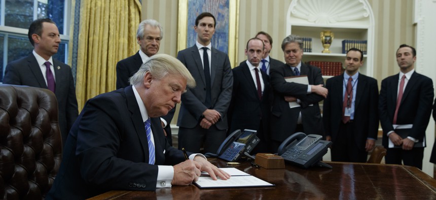 President Donald Trump signs an executive order implementing a federal government hiring freeze, Monday, Jan. 23, 2017, in the Oval Office of the White House in Washington.