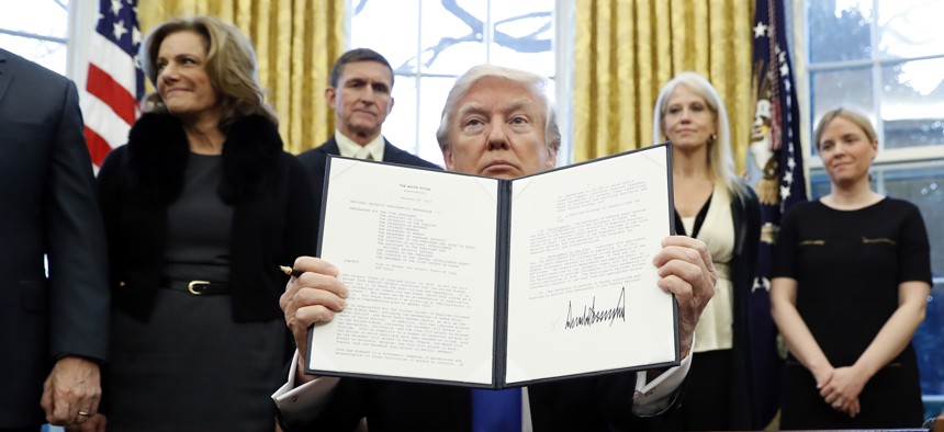President Donald Trump holds up another of his executive actions signed in his first two weeks, this one directing his administration to "develop a comprehensive plan to defeat ISIS." 