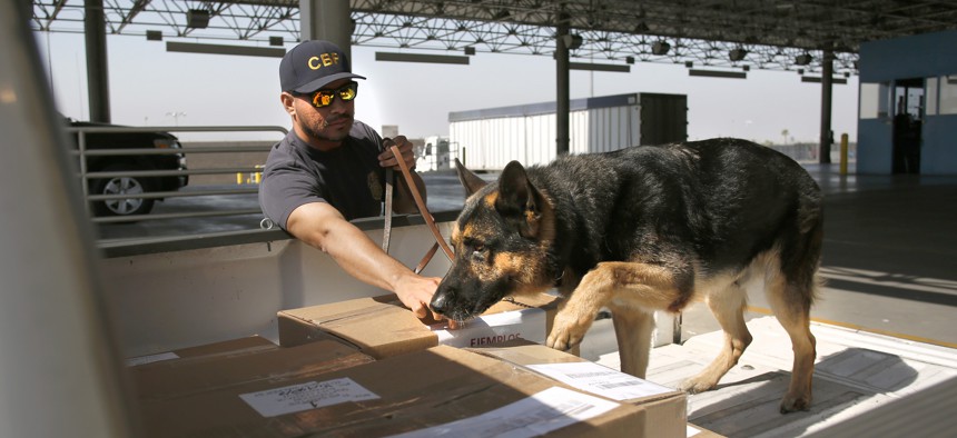 A U.S. Customs and Border Protection officer and his dog screen boxed goods as they are inspected entering the U.S. at the Otay Mesa, Calif., Port of Entry.