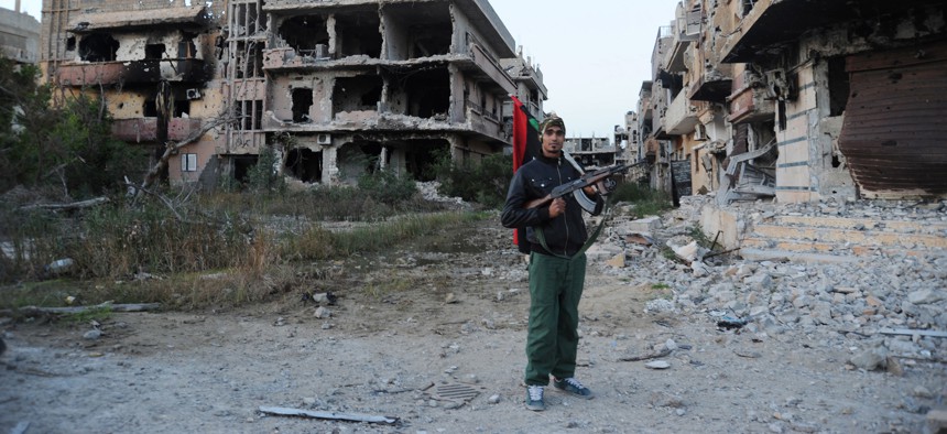 In this February 2016 photo, a civilian fighter holding the Libyan flag stands in front of damaged buildings in Benghazi, Libya.