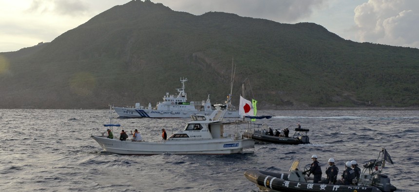 Japanese Coast Guard vessel and boats, rear and right, sail alongside Japanese activists' fishing boat, center with a flag, warning the activists away from a group of disputed islands called Diaoyu by China and Senkaku by Japan, early Sunday Aug 18, 2013.