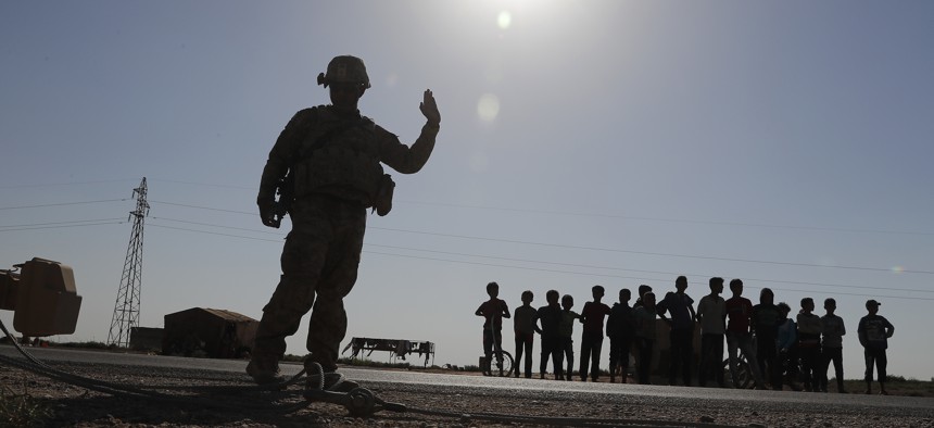 A U.S. silhouetted soldier, left, directs his armored convoy as Syrian children, background, watch, on a road that links to Raqqa city, northeast Syria, Wednesday, July 26, 2017.