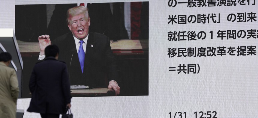 People walk by a huge screen showing a news program reporting U.S. President Donald Trump's State of the Union address, in Tokyo, Wednesday, Jan. 31, 2018. 