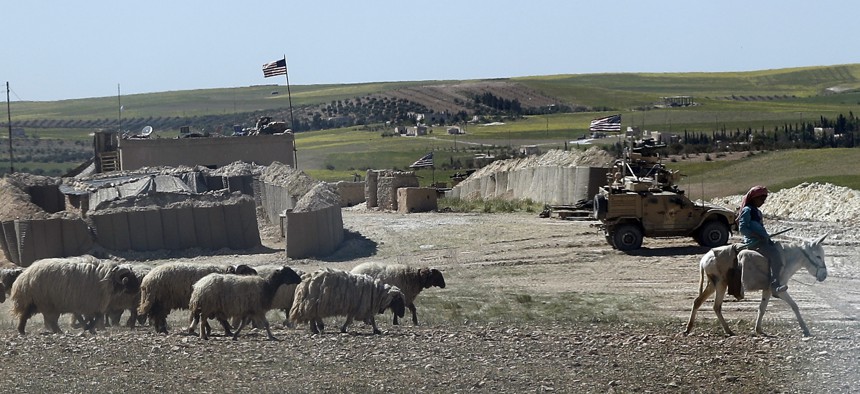 A Syrian shepherd herds his flock, as he passes in front of a newly installed U.S. position near the tense front line between the U.S-backed Syrian Manbij Military Council and the Turkish-backed fighters, in Manbij, north Syria, Wednesday, April 4, 2018. 
