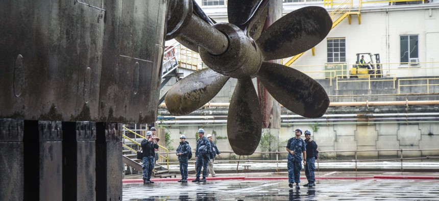 Sailors assigned to the submarine tender USS Frank Cable (AS 40) see their ship's propeller for the first time, as she drains in dry-dock, in Portland, Ore.