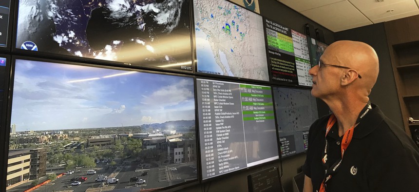 In this Wednesday, July 18, 2018 photo, National Weather Service forecaster Marvin Percha reviews monitors that track satellite and Doppler radar images, as well as his colleagues' forecasts posted on social media, at the agency's operating center in Az.