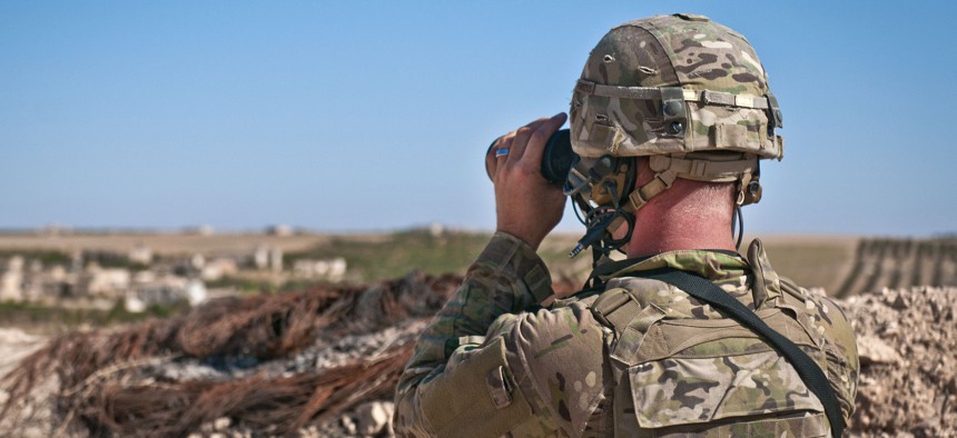 A U.S. soldier looks through binoculars to make visual contact with Turkish soldiers conducting a coordinated, independent patrol along the demarcation line near a village outside Manbij, Syria, July 16, 2018.