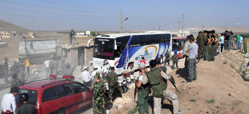 This photo released by the Syrian official news agency SANA, shows Syrian troops, journalists and civilians watching as buses evacuate people from two pro-government villages, the crossing between Aleppo and Idlib provinces July 18, 2018.