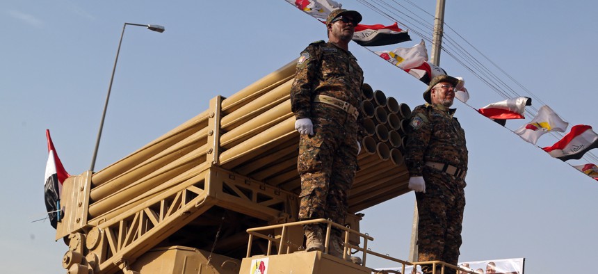 Members of the Abbas combat squad, a Shiite militia group, ride under militia and national flags atop a mobile rocket launcher during a military parade in Basra, 340 miles (550 kilometers) southeast of Baghdad, Iraq, Saturday, Sept. 26, 2015.