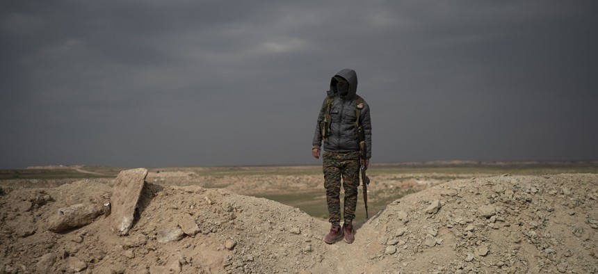 A U.S.-backed Syrian Democratic Forces, or SDF, fighter stands in the desert outside the village of Baghouz, Syria, Thurs., Feb. 14, 2019. 