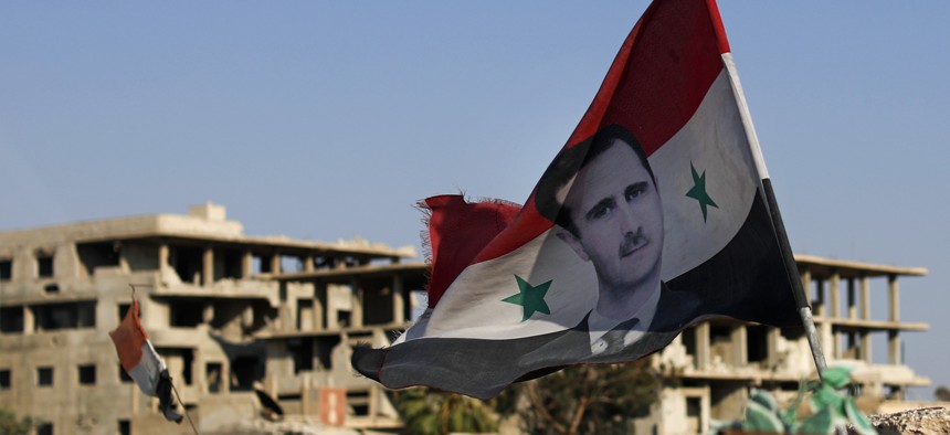 In this July 15, 2018 file photo, a Syrian national flag with a picture of Syrian President Bashar Assad flies at an Army check point, in the town of Douma in the eastern Ghouta region, near Damascus, Syria. 