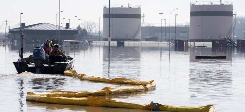 In this March 18, 2019 file photo released by the U.S. Air Force, environmental restoration employees deploy a containment boom from a boat on Offutt Air Force Base in Nebraska, as a precautionary measure for possible fuel leaks in the flooded area.